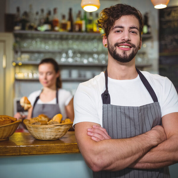Smiling waiter standing with arms crossed in café